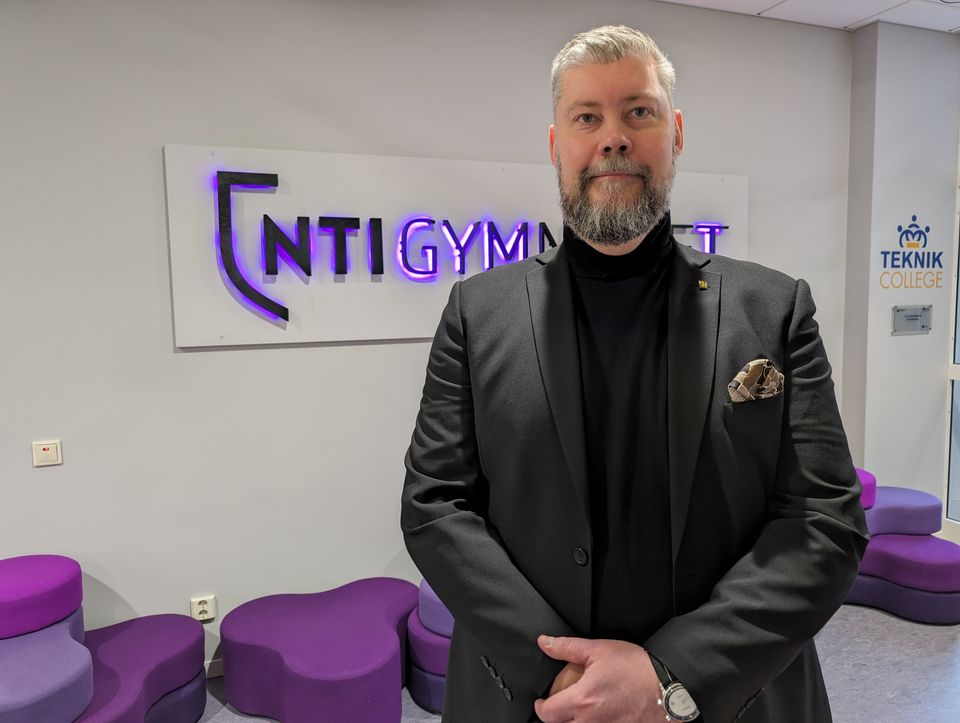 Rektor Anders Tegerhult på NTI Västerås står framför NTI:s logga på väggen.