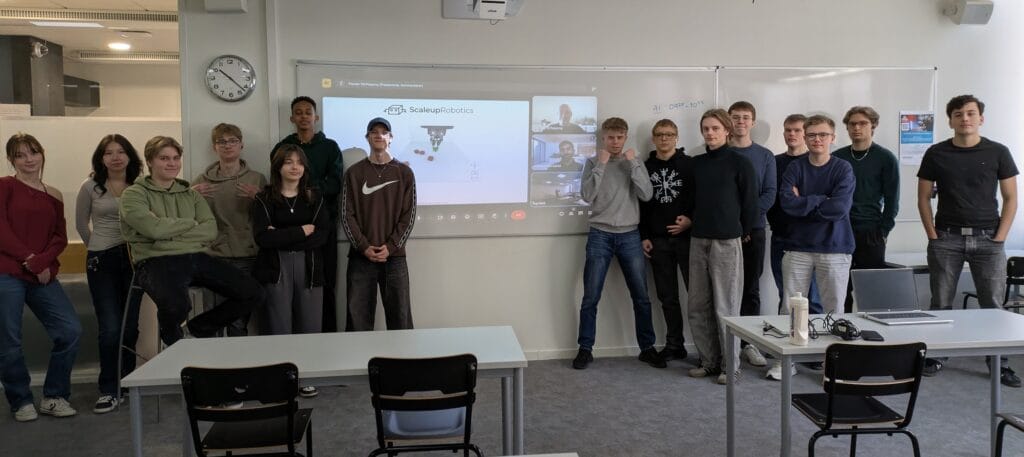 En grupp elever från NTI Gymnasiet står framför en whiteboard där det står Scaleup Robotics.
