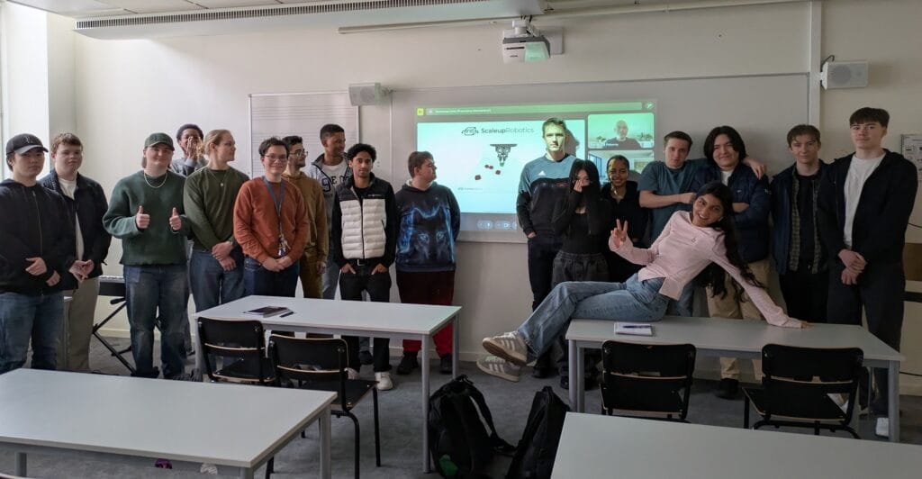 En grupp elever från NTI Gymnasiet står framför en whiteboard där det står Scaleup Robotics.