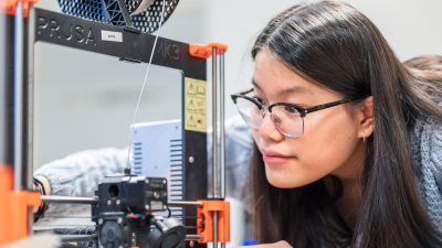 Elev på NTI Gymnasiet står vid en 3D-printer i Makerspace och tittar noggrant på den blivande produkten som skrivs ut