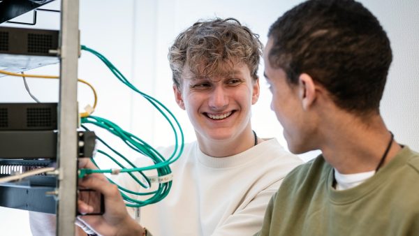 Två elever står i ett IT-labb vid servrar och kopplar samman olika nätverksladdar på IT-programmet
