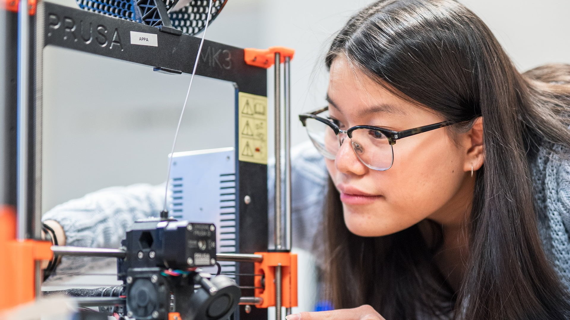 En elev studerar sin prototyp som hon håller på att ta fram med hjälp av en 3D-printer i makerspace