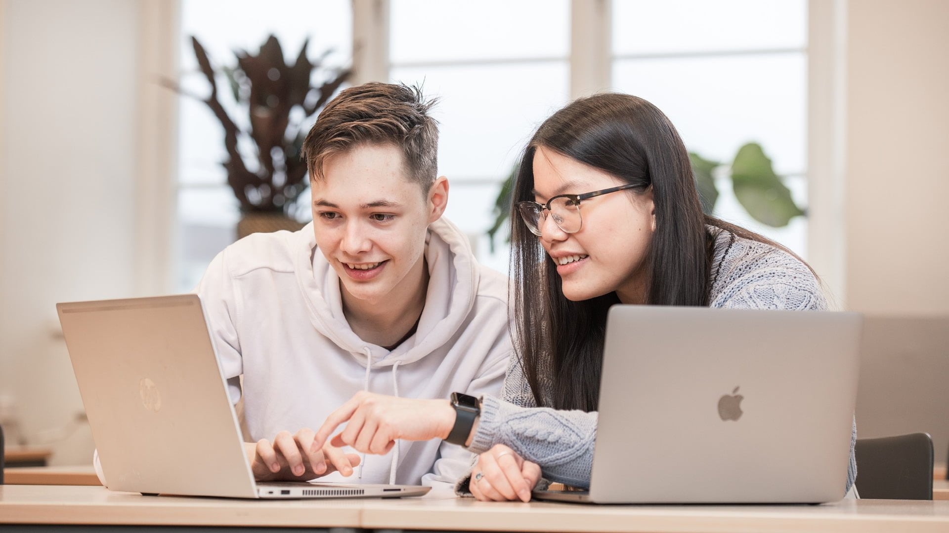 Två elever sitter vid sina datorer i klassrummet och samarbetar kring en uppgift på teknikprogrammet