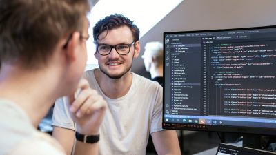 En lärare och en elev sitter framför en stor skärm med massor av kod på, läraren hjälper eleven att programmera.