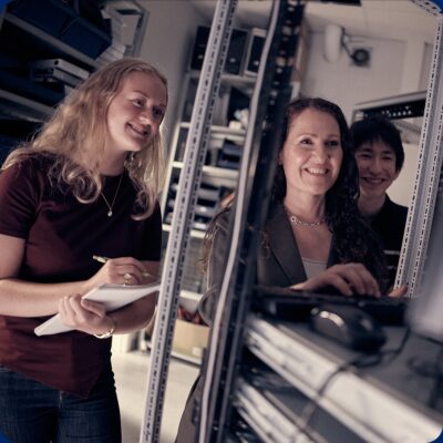 Elev antecknar medan en lärare visar serverutrustning för två elever.