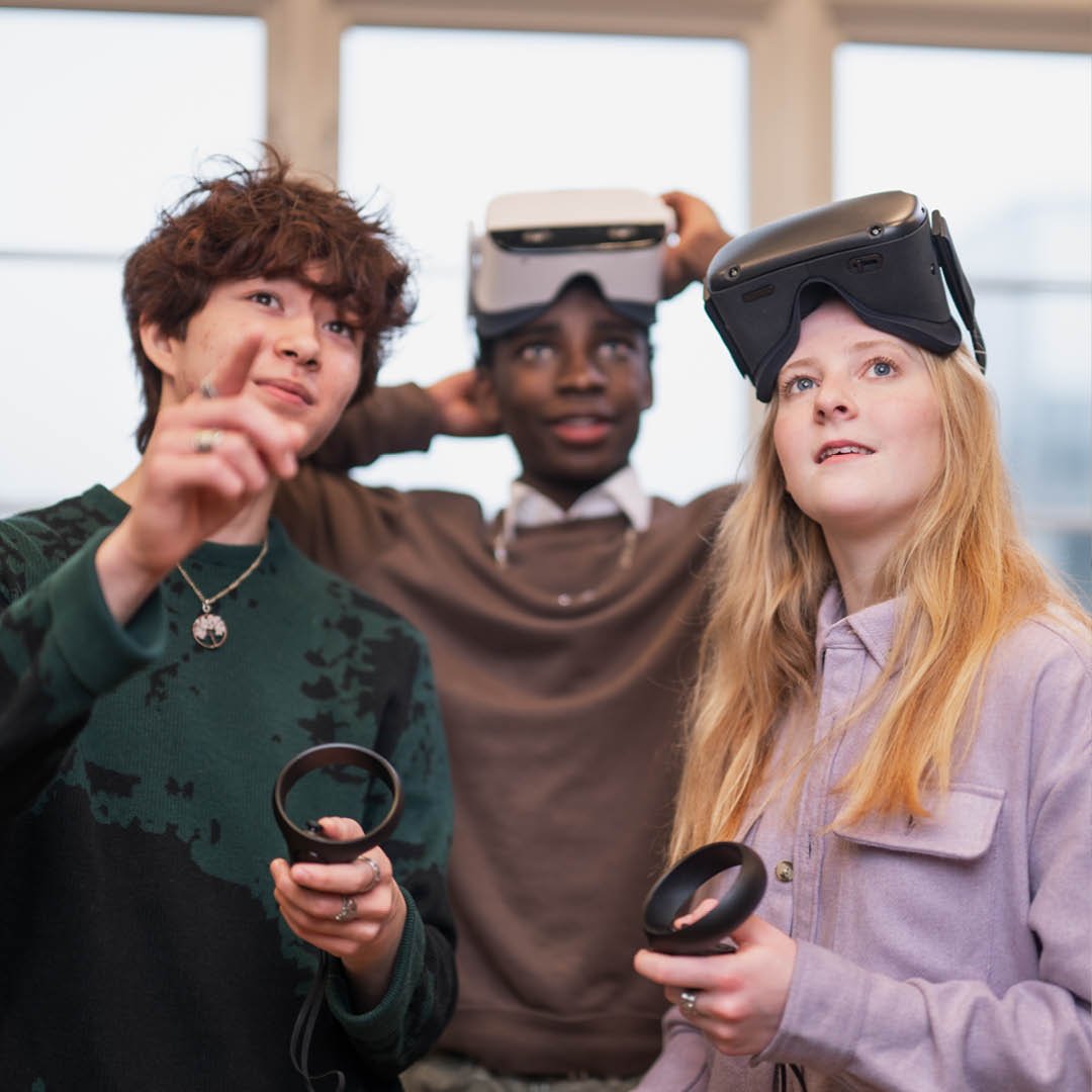 3 elever spelar med VR-utrustning och tittar upp på en VR-skärm