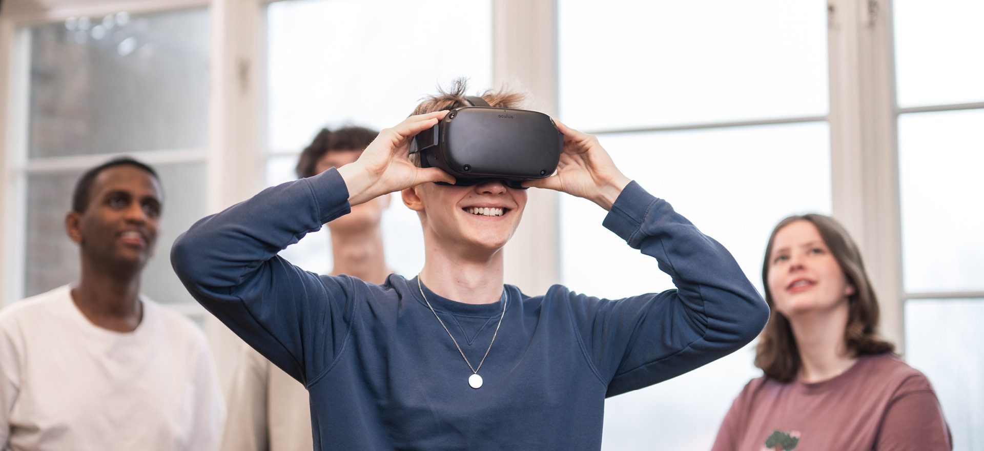 4 elever står och spela med VR. Killen längst fram har på sig VR-glasögon och de andra står bakom och tittar upp på en skärm som visar vad han ser.