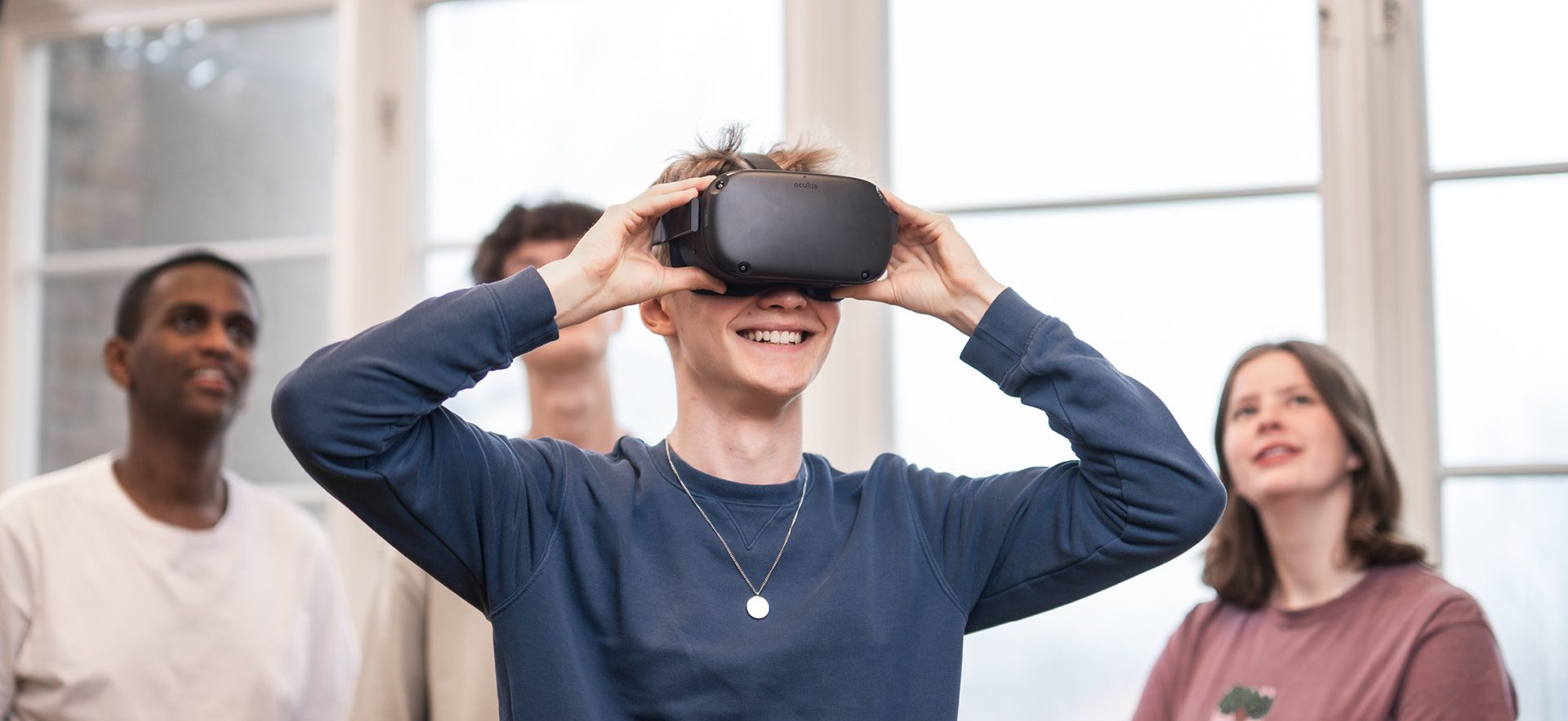 4 elever står och spela med VR. Killen längst fram har på sig VR-glasögon och de andra står bakom och tittar upp på en skärm som visar vad han ser.