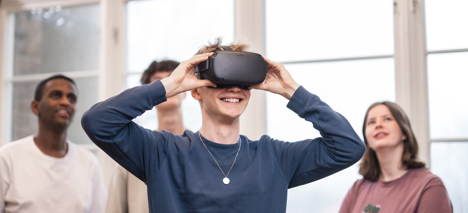 4 elever står och spela med VR. Killen längst fram har på sig VR-glasögon och de andra står bakom och tittar upp på en skärm som visar vad han ser.