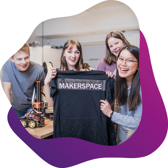 4 elever i makerspace tittar in i kameran och håller upp en tshirt som de tryckt ordet makerspace på