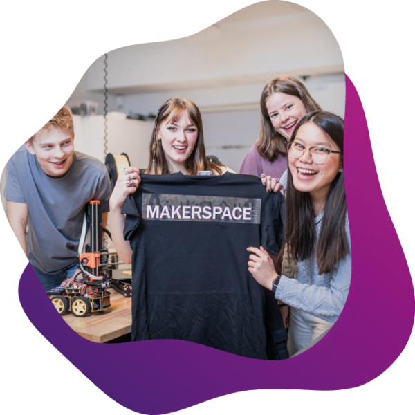 4 elever i makerspace tittar in i kameran och håller upp en tshirt som de tryckt ordet makerspace på.