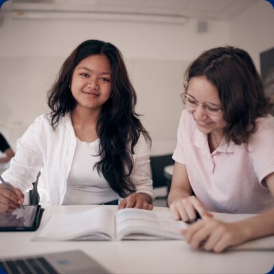 Två glada elever i klassrum som pluggar tillsammans.