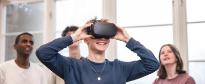 4 elever står och spela med VR. Killen längst fram har på sig VR-glasögon och de andra står bakom och tittar upp på en skärm som visar vad han ser.