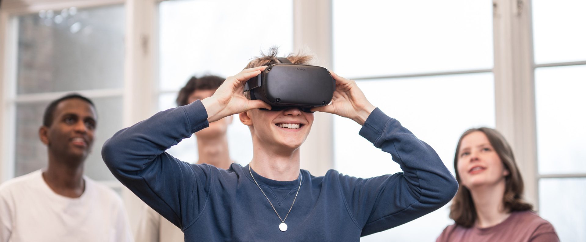 4 elever står och spela med VR. Killen längst fram har på sig VR-glasögon och de andra står bakom och tittar upp på en skärm som visar vad han ser.