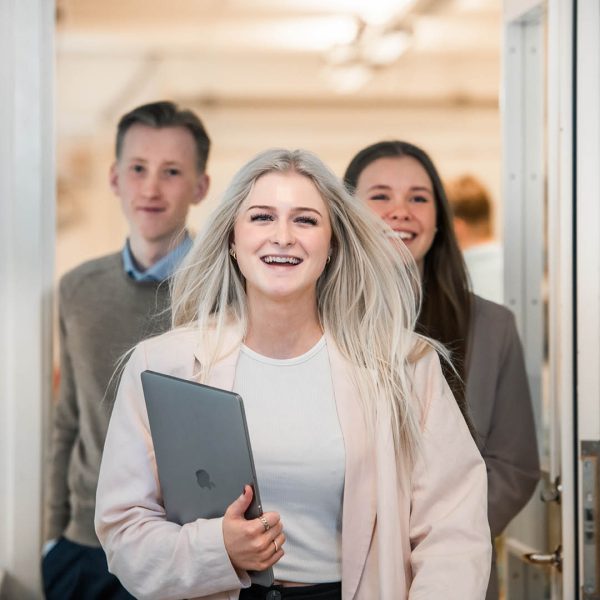 Tre elever går i en korridor med dator i handen