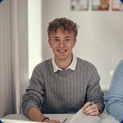 En glad elev som bläddrar i en juridikbok samtidigt som han tittar in i kameran.
