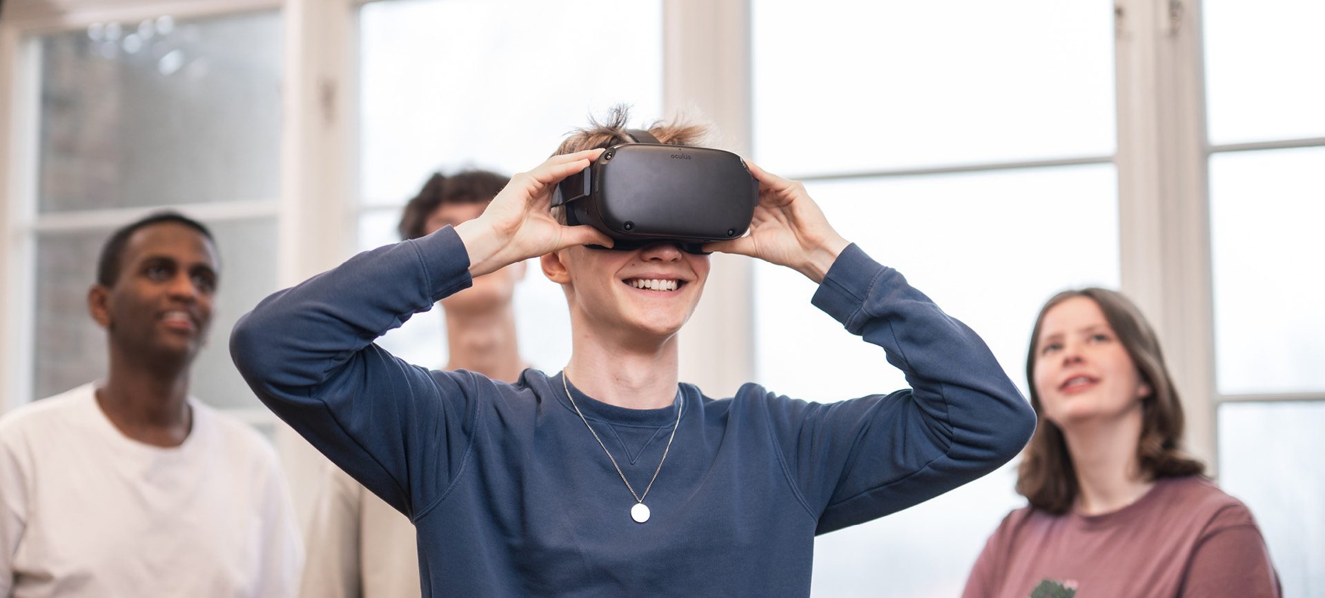 4 elever står och spela med VR. Killen längst fram har på sig VR-glasögon och de andra står bakom och tittar upp på en skärm som visar vad han ser.