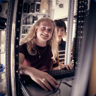 Elev arbetar vid en dator i ett serverutrustning medan en annan elev står bakom.