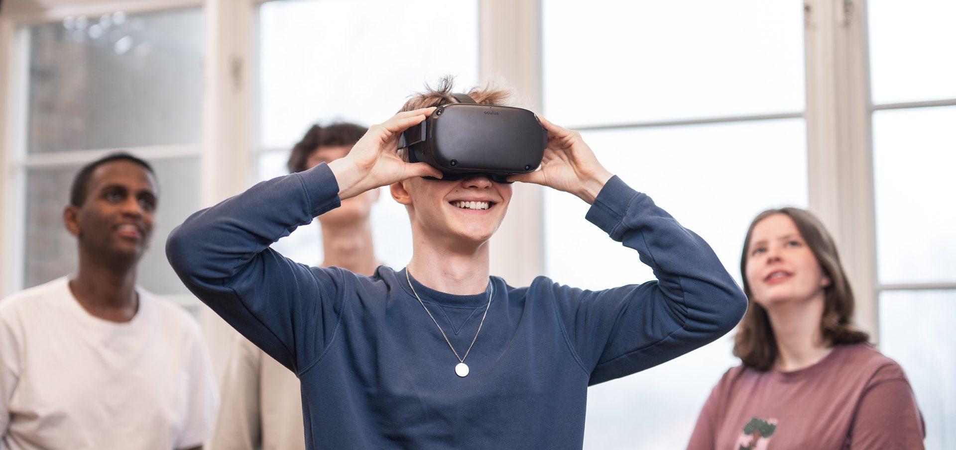 4 elever står och spela med VR. Killen längst fram har på sig VR-glasögon och de andra står bakom och tittar upp på en skärm som visar vad han ser.