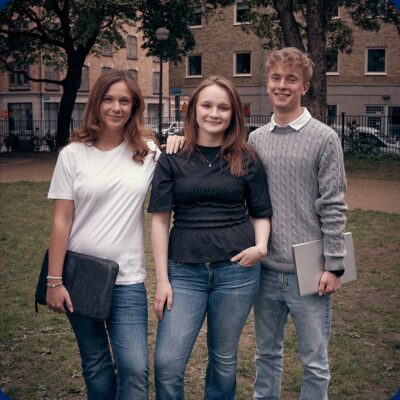 Tre elever i parken utanför skolan med datorer i handen.