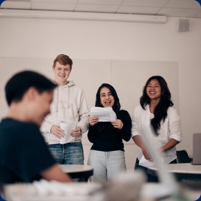 Tre glada elever som håller i redovisning framför klassen.